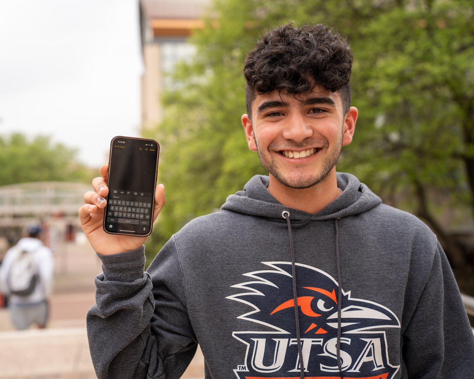 Student smiling and holding phone towards camera showing keyboard open