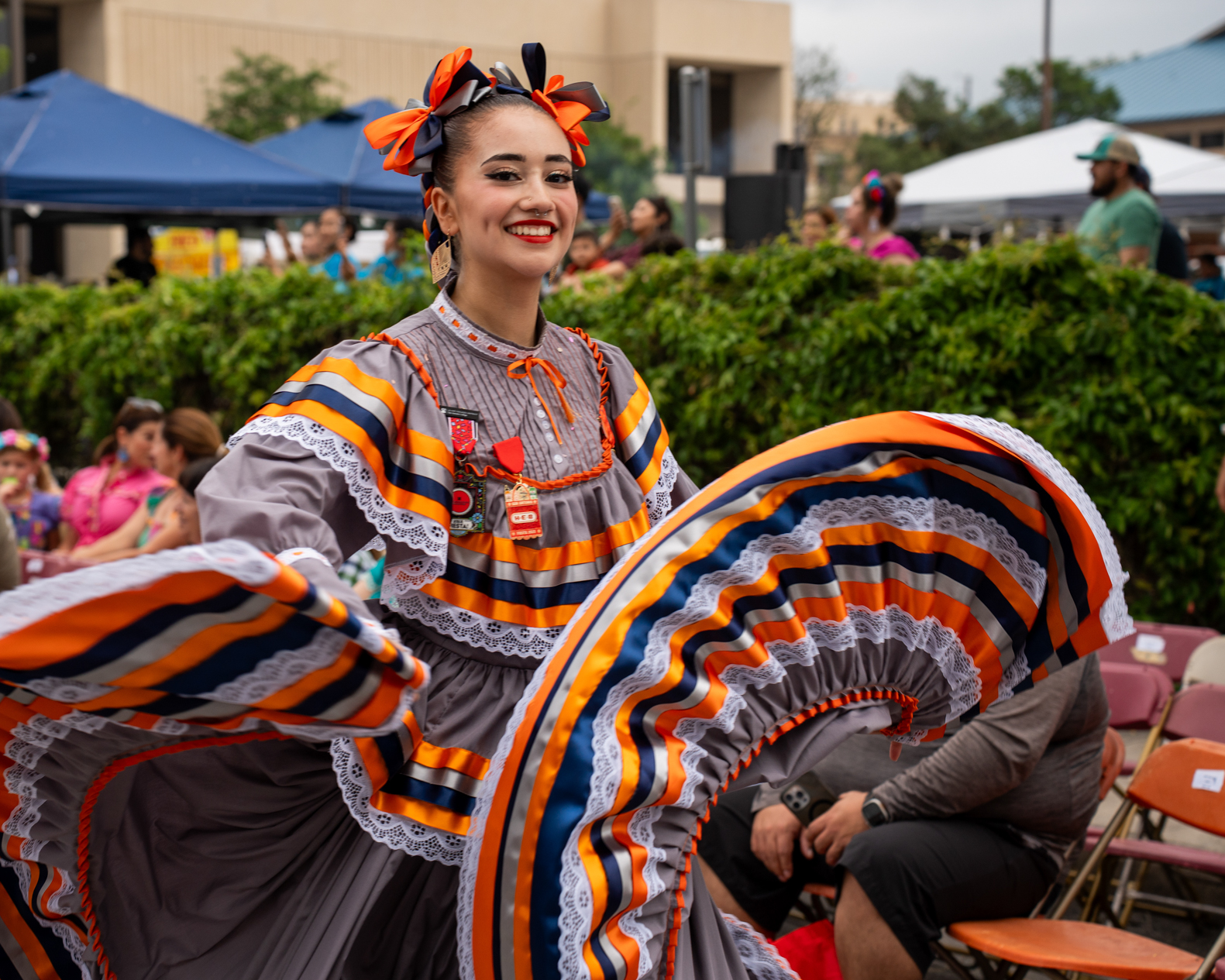 A person wearing vibrant costumes for Mexican Folklorico dance while walking in a parade