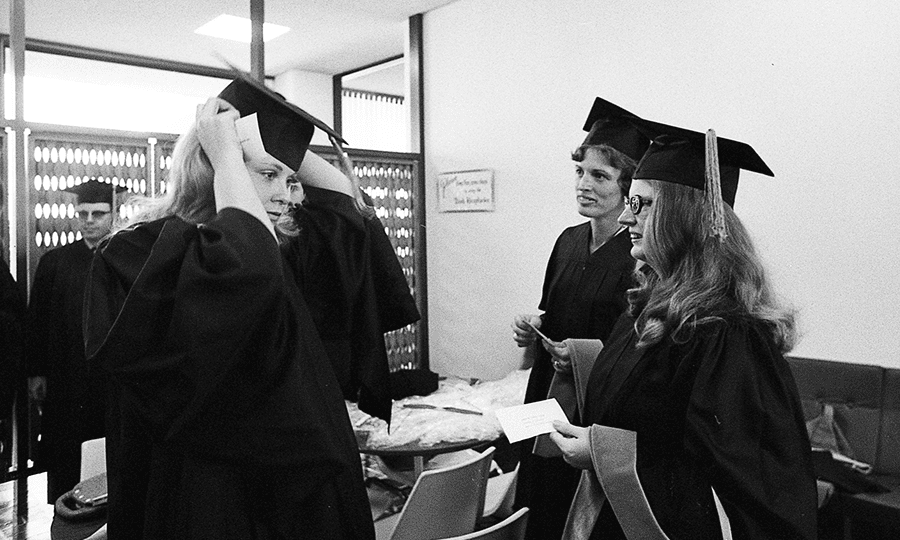 Toni Rahm fits a mortarboard on her head, with Karen Kyritz (in background) and Susan Bolado guiding her progress, prior to UTSA’s first commencement ceremonies on August 18, 1974.