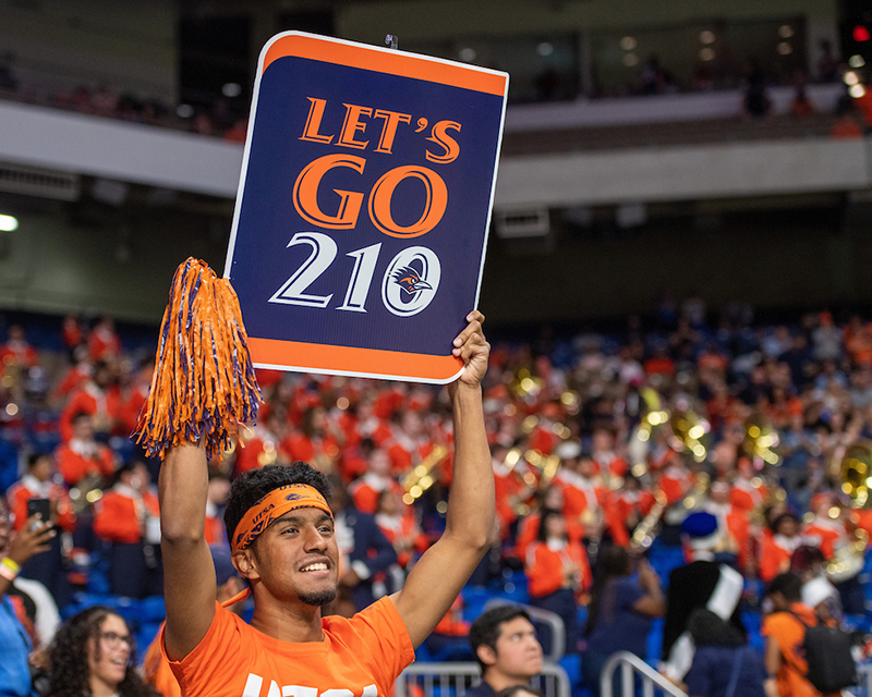 A student holds up a "Let's Go 210" sign in a crowded stadium.