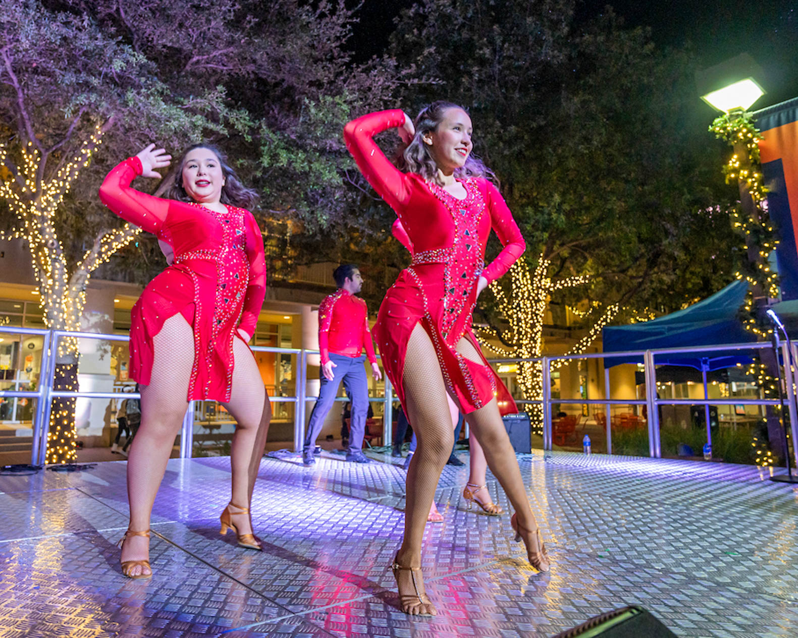 Two students performing on a stage in front of trees covered in lights