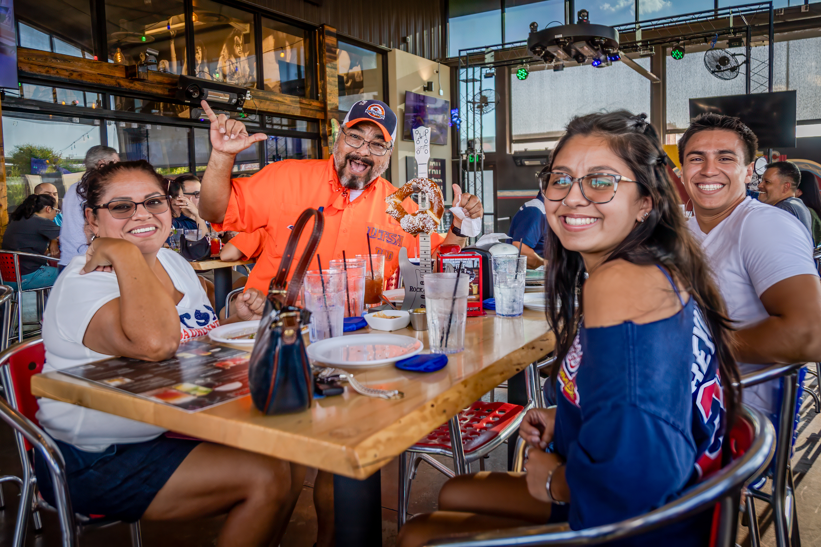A family siting at a table in a restaurant posing for a photo with the father holfing a birds up gesture