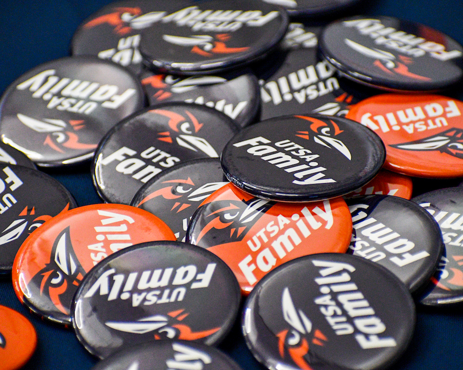 A pile of orange and blue buttons that say UTSA Family with a Roadrunner Heat