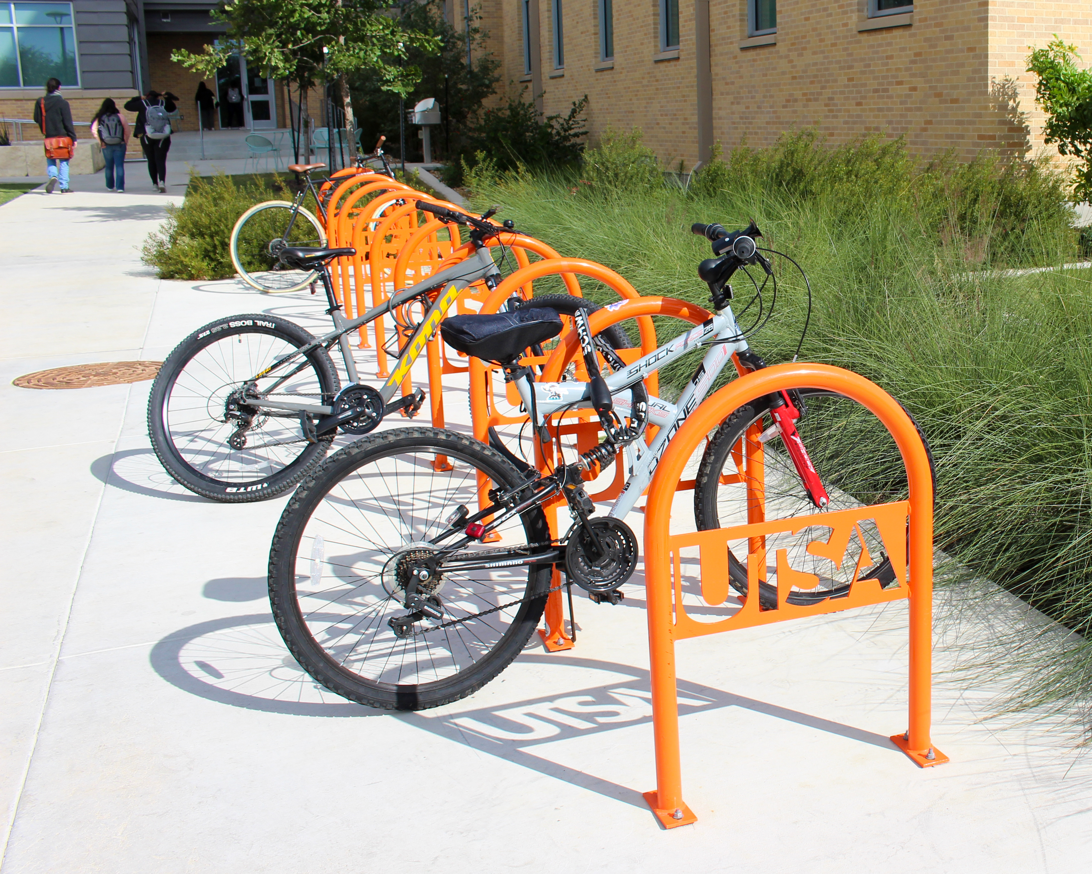 Two bicycles parked in an orange UTSA bike rack on campus.