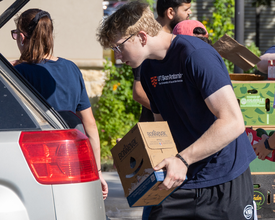 A young woman wearing a navy shirt with 'UTSA Sciences' across the front holds up a cell phone