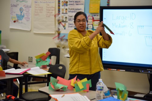 a female instructor holds a paper showing a class of students how to complete it