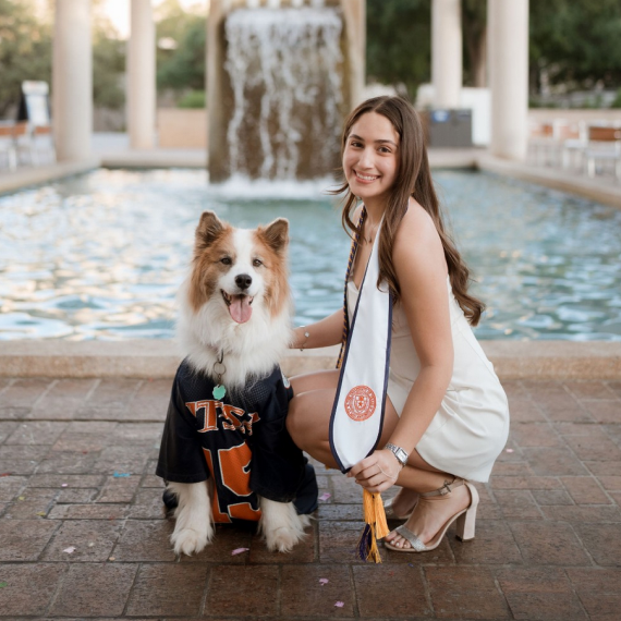 UTSA graduate posing with her dog in front of the fountain.