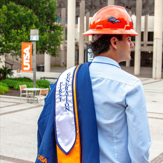 UTSA graduate wearing a hard hat while holding his grown.