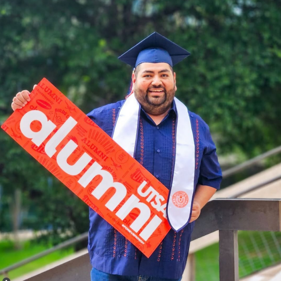 UTSA graduate holding a sign that says 'UTSA Alumni'
