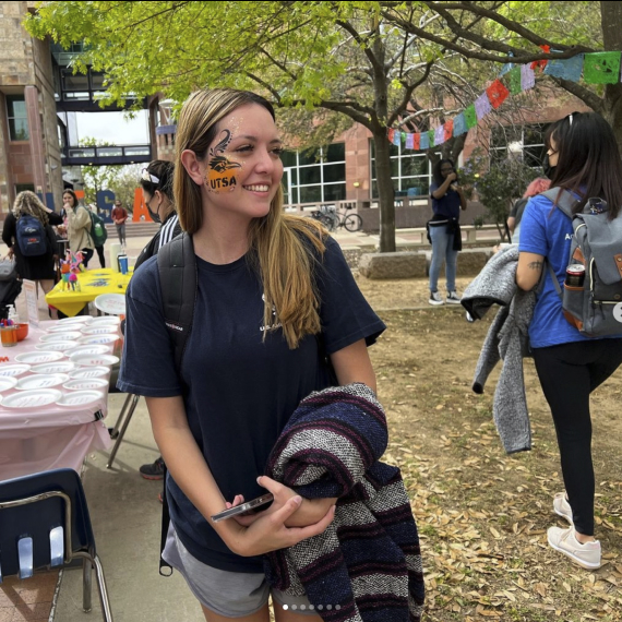 Smiling blonde female student with UTSA Rowdy face paint on her cheek for a UTSA Fiesta event downtown