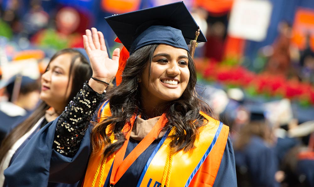 Student waving at the camera in cap and gown