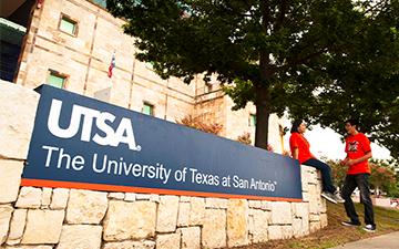 Two students sitting on a UTSA sign