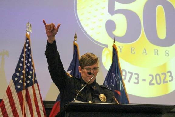 Lemmonds at podium giving roadrunner sign with her hand