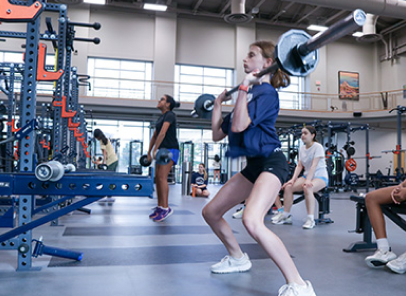 Young girl performing a squat while holding a weighted barbell.
