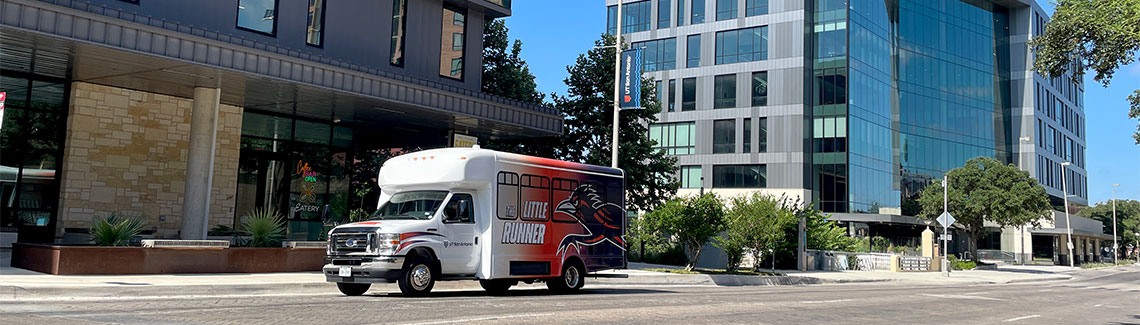 A small bus with Little Runner and the Roadrunner logo driving on a street in the city.