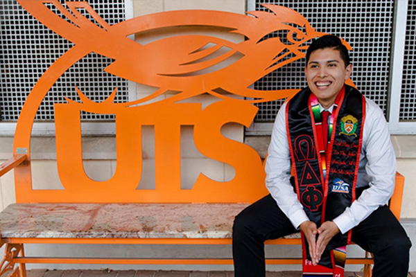 UTSA graduate sitting on one of the UTSA benches on campus