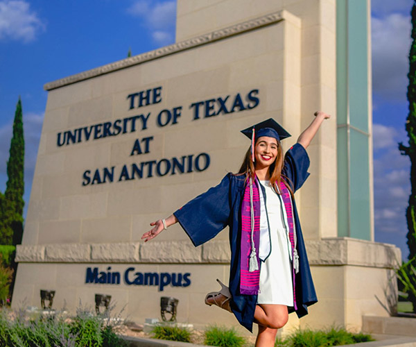 UTSA graduate in full regalia taking a photo in front of the UTSA monument