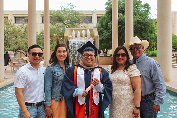 UTSA graduate and his family taking a photo in front of the sombrilla fountain