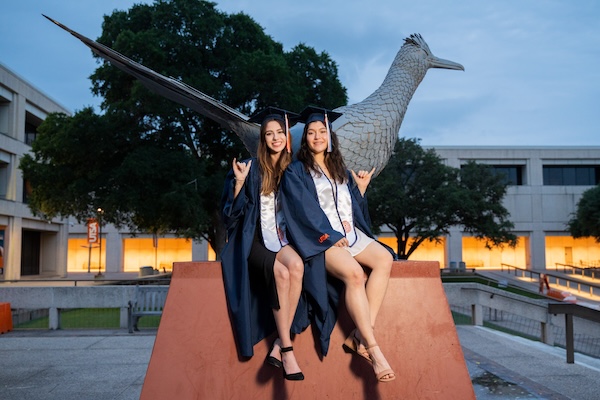 UTSA graduate in full regalia in front of the roadrunner statue on campus