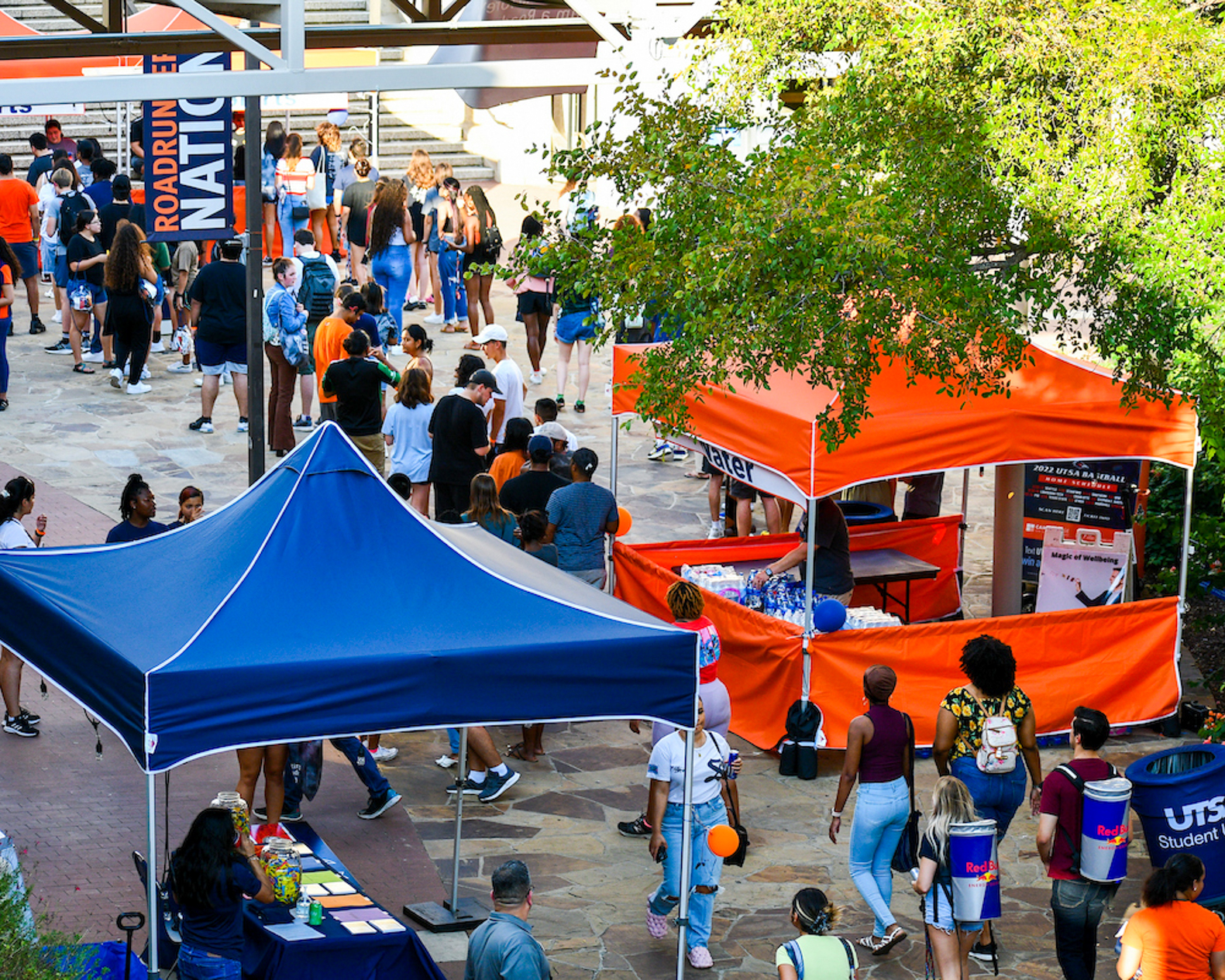 A group of students are gathering on the walkway stopping at activity booths.