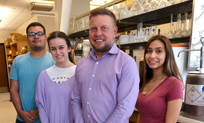 a professor poses with three students in a research lab