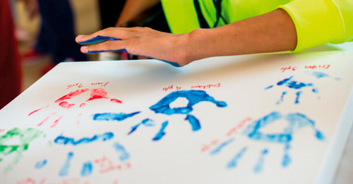 A child prepares to press their painted alongside other handprints.