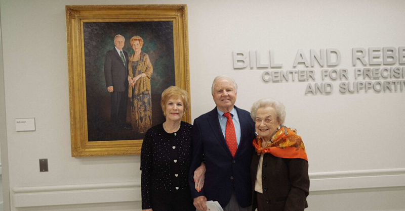 Rebecca Reed, Bill Reed and Ann Biggs are shown in front of a portrait of the Reeds at the Biggs Institute
