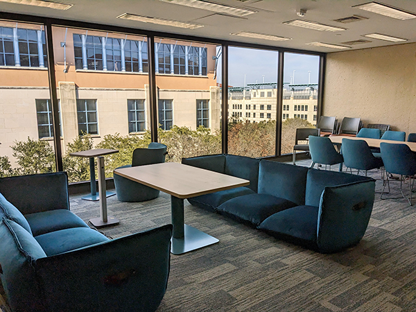 View of third floor jpl collaboration space, two blue lounge sofas with a small work table in between. At back, a large window shows Business building during daytime.