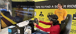 Girl seated holding a steering wheel controller wearing a VR headset at a Drive Sober event.