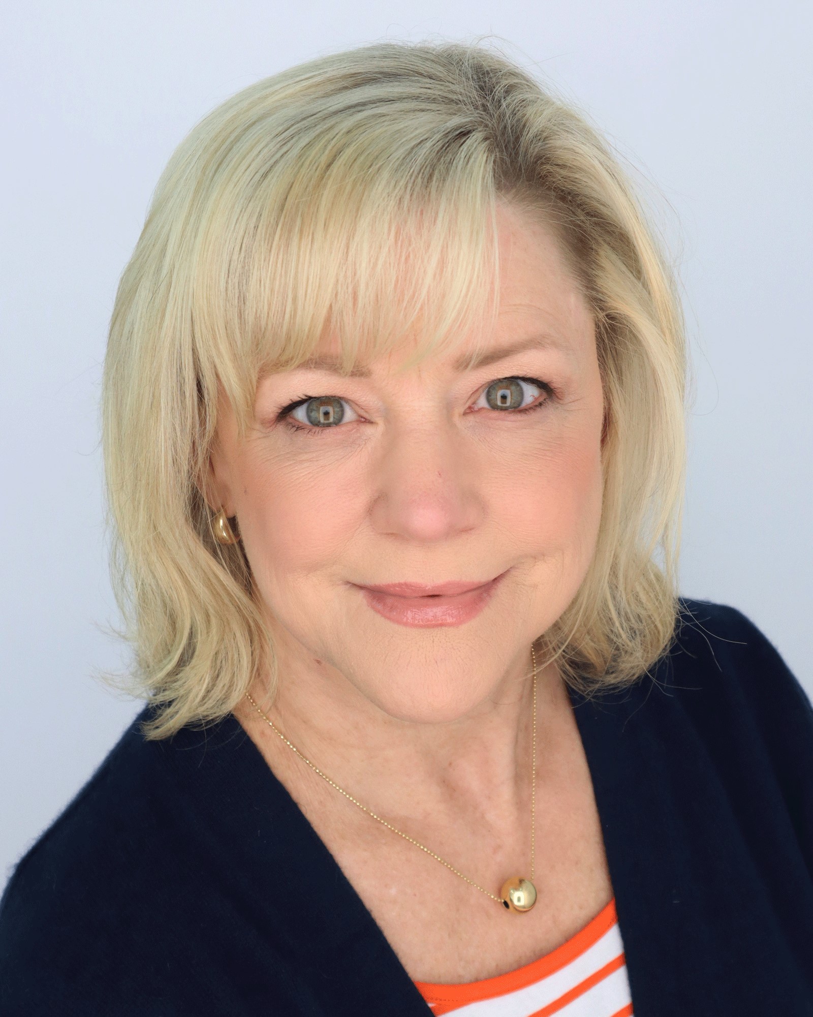 headshot of Carrie Charley wearing a dark business suit and a orange and white striped top.