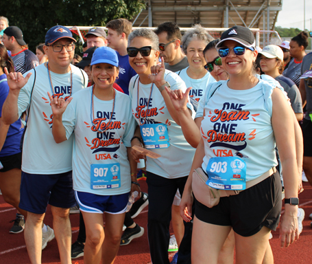 four corporate cup participants outside giving the rowdy hand symbol, smiling wearing corporate cup t-shirts.