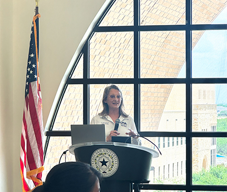 Chief Scheonborn speaking behind a state of texas podium holding a microphone looking at the audience at the SA BIT Coalition event..