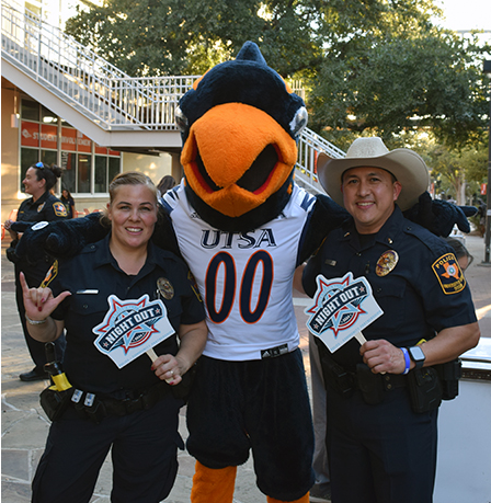 Rowdy mascot person standing in the middle of two police officers - one male, one female outside on campus near Student Union.