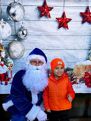 Blue Santa squatting down next to child wearing orange jacking and beenie.