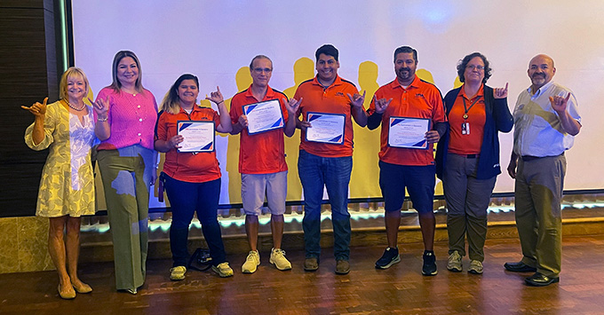 Parking enforcement team on stage posting for photo holding certificates in one hand and making the bird up gesture with their other hands..