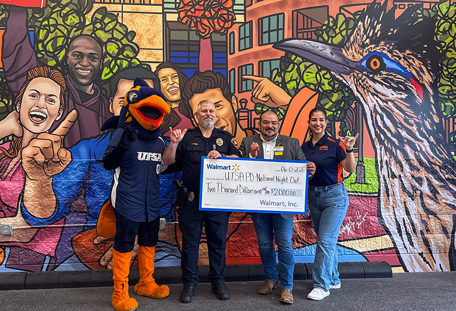 Rowdy mascot, two men and a woman posing in front of a mural, two men are holding a large check from Walmart in amount 2,000 dollars to UTSA-PD NNO..