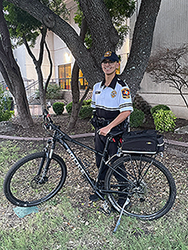 Christian Andrade Santos standing outside on campus hold on to a bike in front of a tree.