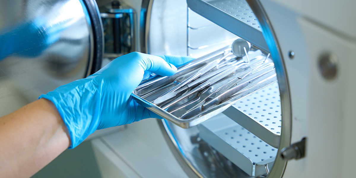 Gloved technician placing a tray of surgical instruments into sterilization equipment