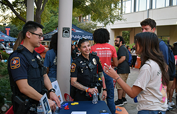 Two UTSAPD officers speak with students at a campus table about safety resources during National Night Out.