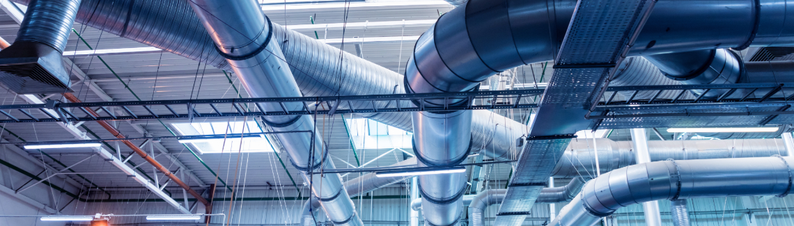 Ceiling of an industrial building showing large ventilation ducts in cold blue lighting.