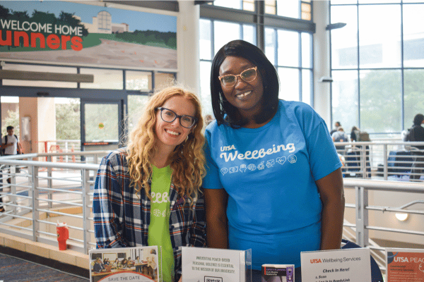 two women in UT San Antonio Wellbeing shirts, tabling for PEACE