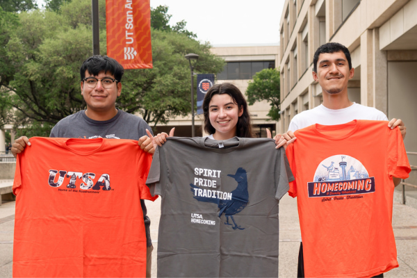 Three students holding up three different Homecoming and Family Weekend shirts.