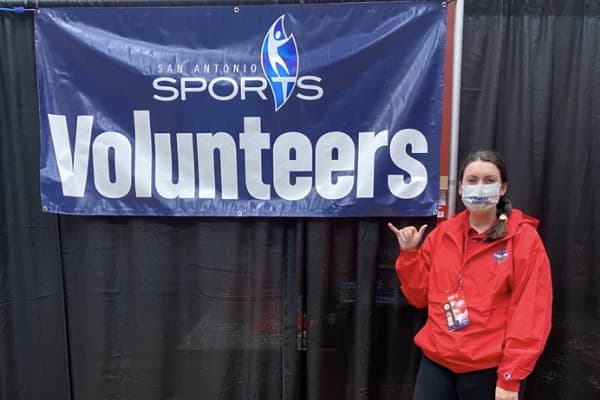 Student throws up the Rowdy hand sign in front of a Vounteer Sports banner