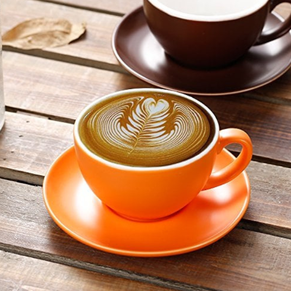 An orange cup and saucer filled with coffee, a browm cup and saucer in the background to the upper right