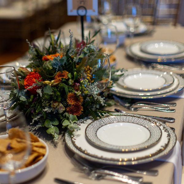 A large table with a floral centerpiece and set with formal place settings including plates, utensils, and glassware