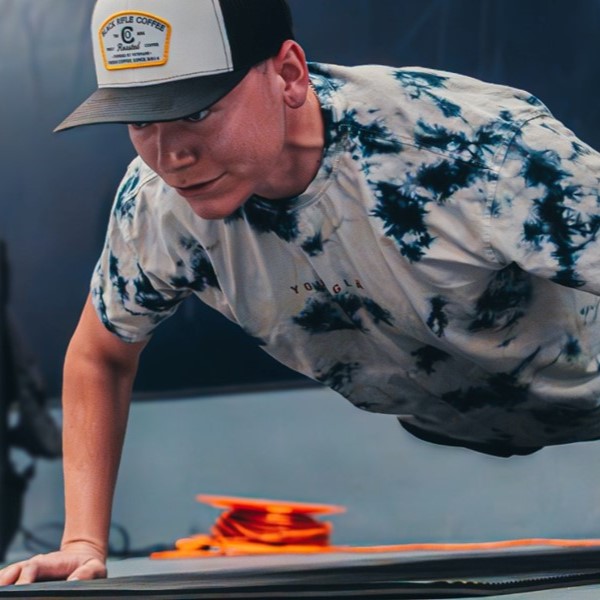 Close up of a student in a black and grey tye dye tee and a baseball cap doing a push up.