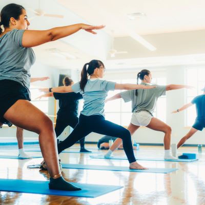 Students in a line standing at warrior pose in a bright studio room.