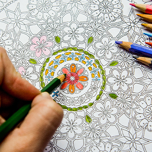 Closeup of a hand using a green colored pencil to color in a coloring worksheet.