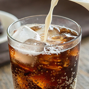 A glass filled with soda and ice, with cream being poured into the glass.