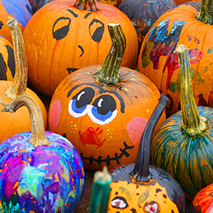 Many pumpkins, some painted with faces and some with lots of different colors of paint on them.
